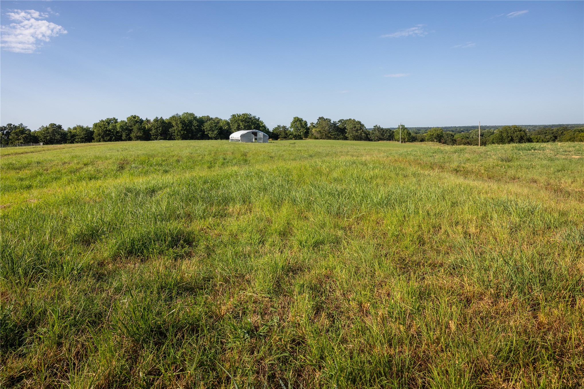 0 West Dunkin Road Cushing, OK 74023 - Photo 23 of 62 Expansive pastoral acreage with lush green fields, mature tree line bordering the property, and a residential structure visible in the distance