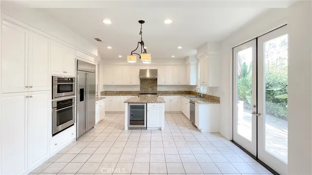 a kitchen with stainless steel appliances kitchen island granite countertop a refrigerator a sink a stove and white cabinets with wooden floor