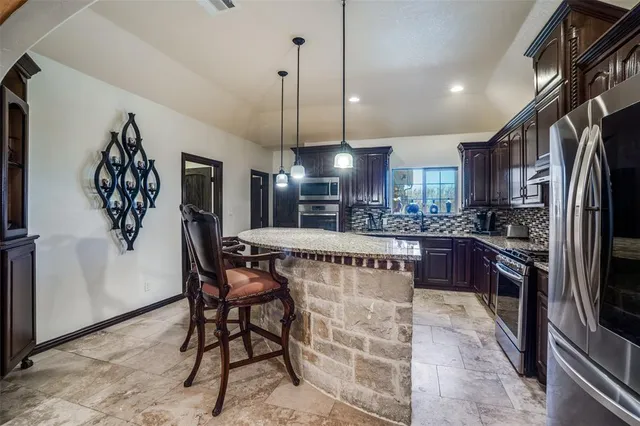 a kitchen with stainless steel appliances kitchen island granite countertop a refrigerator a stove a oven with a dining table and chairs