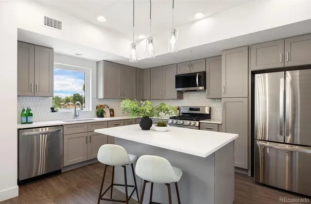 a kitchen with stainless steel appliances granite countertop a refrigerator a sink dishwasher a stove and a dining table with wooden floor