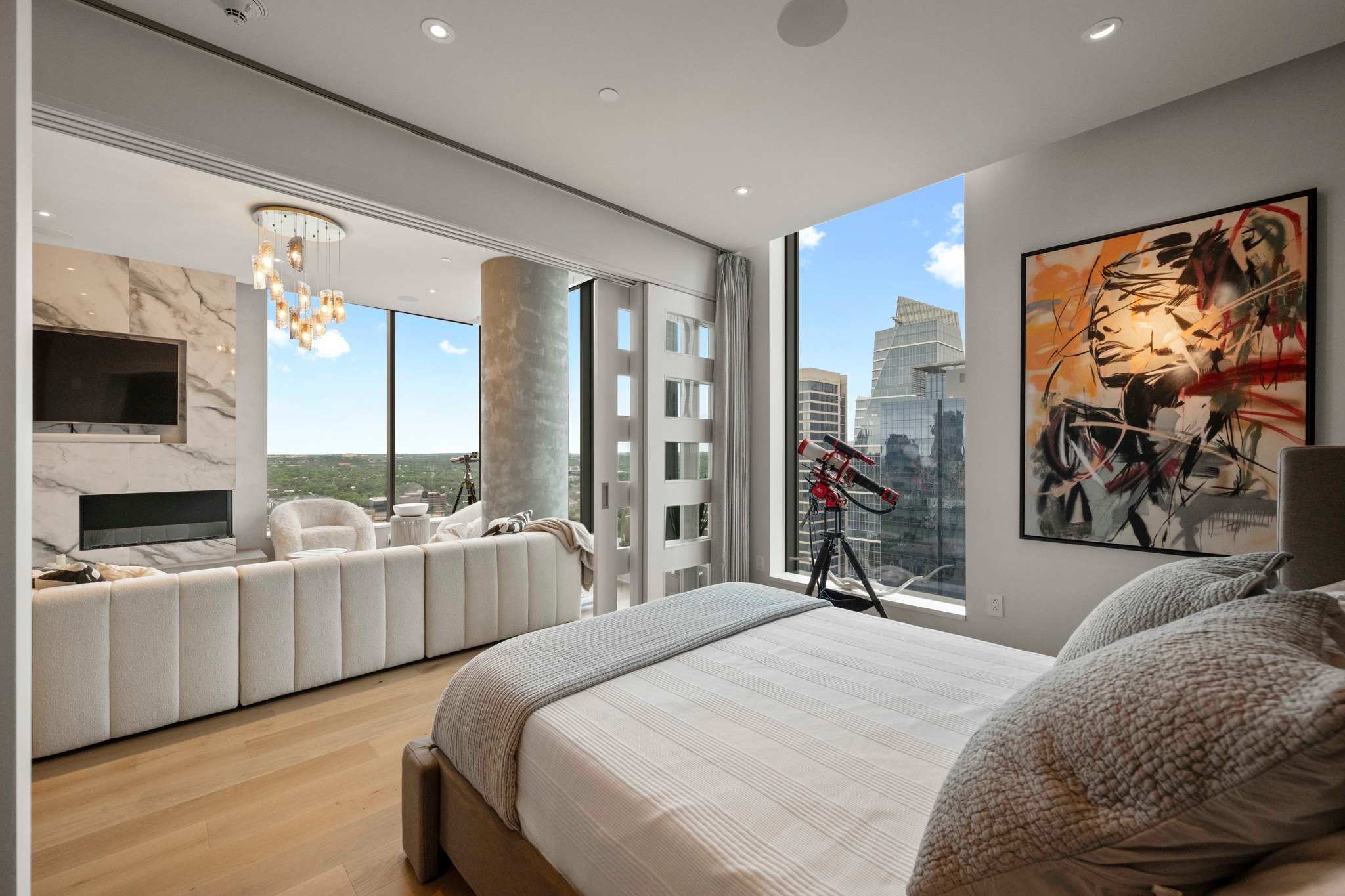 210 Lavaca Street, Unit 2706 Austin, TX 78701 - Photo 18 of 32 Expansive bedroom featuring light wood-finish flooring, full-height windows, a built-in electric fireplace with marble surround, recessed ceiling lighting, and a modern chandelier