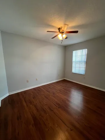 an empty room with wooden floor fan and windows