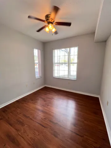an empty room with wooden floor fan and windows