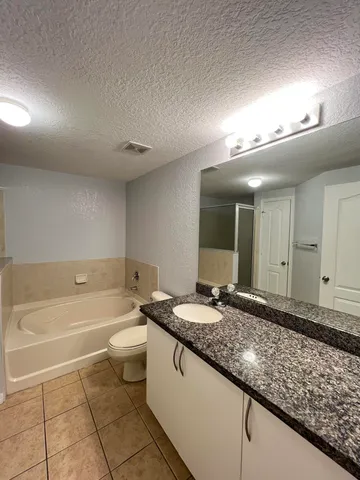 a bathroom with a granite countertop sink a toilet a mirror and bathtub