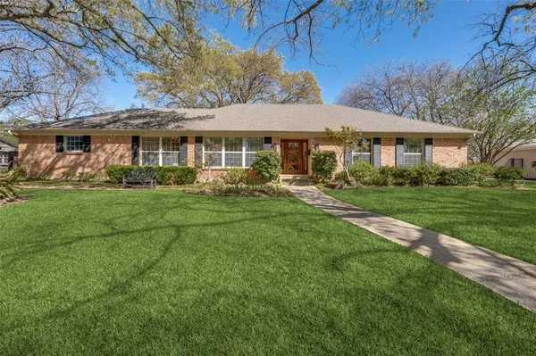 a view of a white house with a big yard and potted plants and large trees