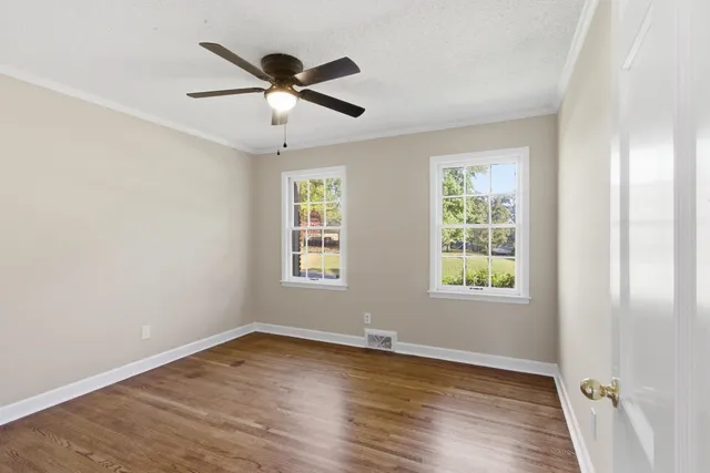 an empty room with chandelier fan and windows