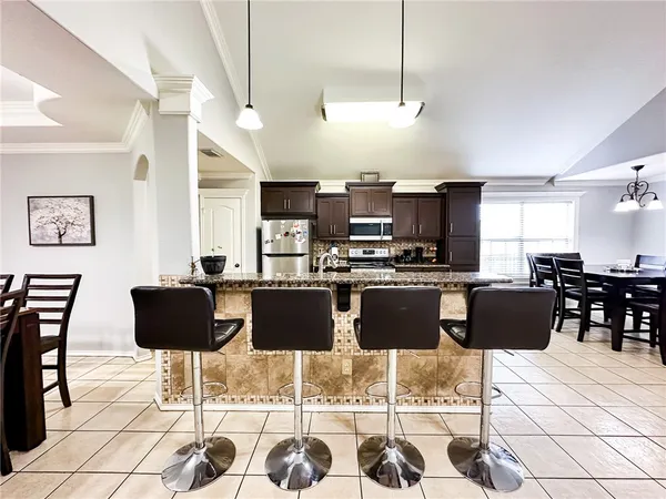 a kitchen with stainless steel appliances kitchen island granite countertop a dining table chairs and a refrigerator