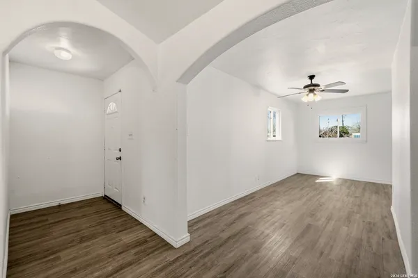 an empty room with wooden floor a chandelier fan and windows
