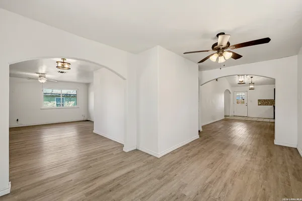 an empty room with wooden floor chandelier fan and windows