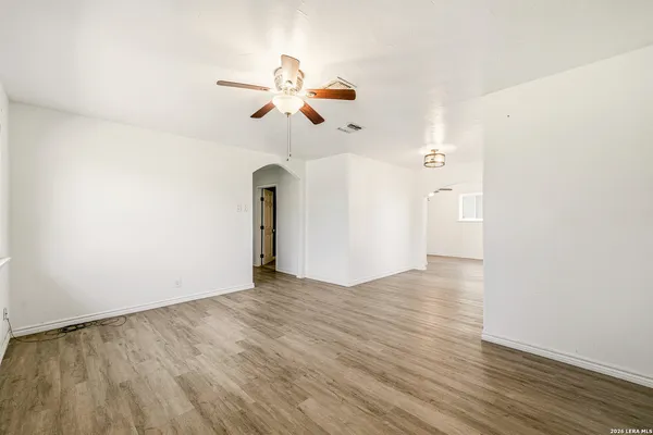 a view of an empty room with wooden floor and a ceiling fan