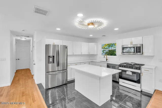 a kitchen with stainless steel appliances granite countertop a refrigerator a stove a sink a oven and a refrigerator with wooden floor