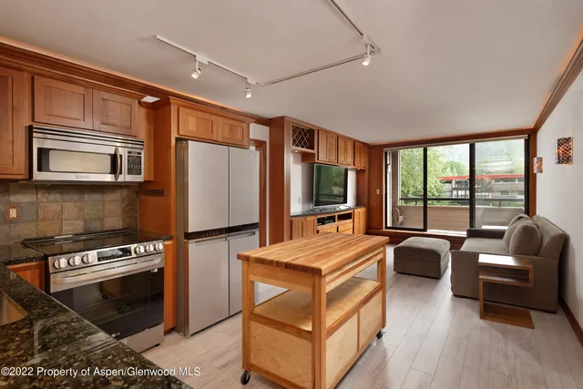 a kitchen with stainless steel appliances granite countertop a refrigerator stove microwave and couches with wooden floor