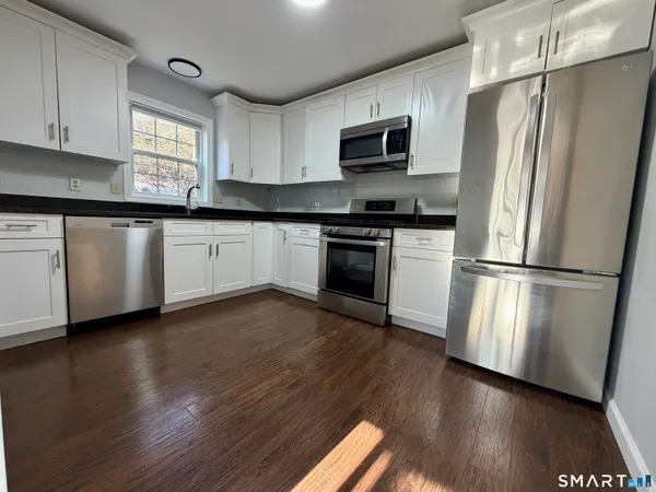 a kitchen with granite countertop wooden floors stainless steel appliances and window