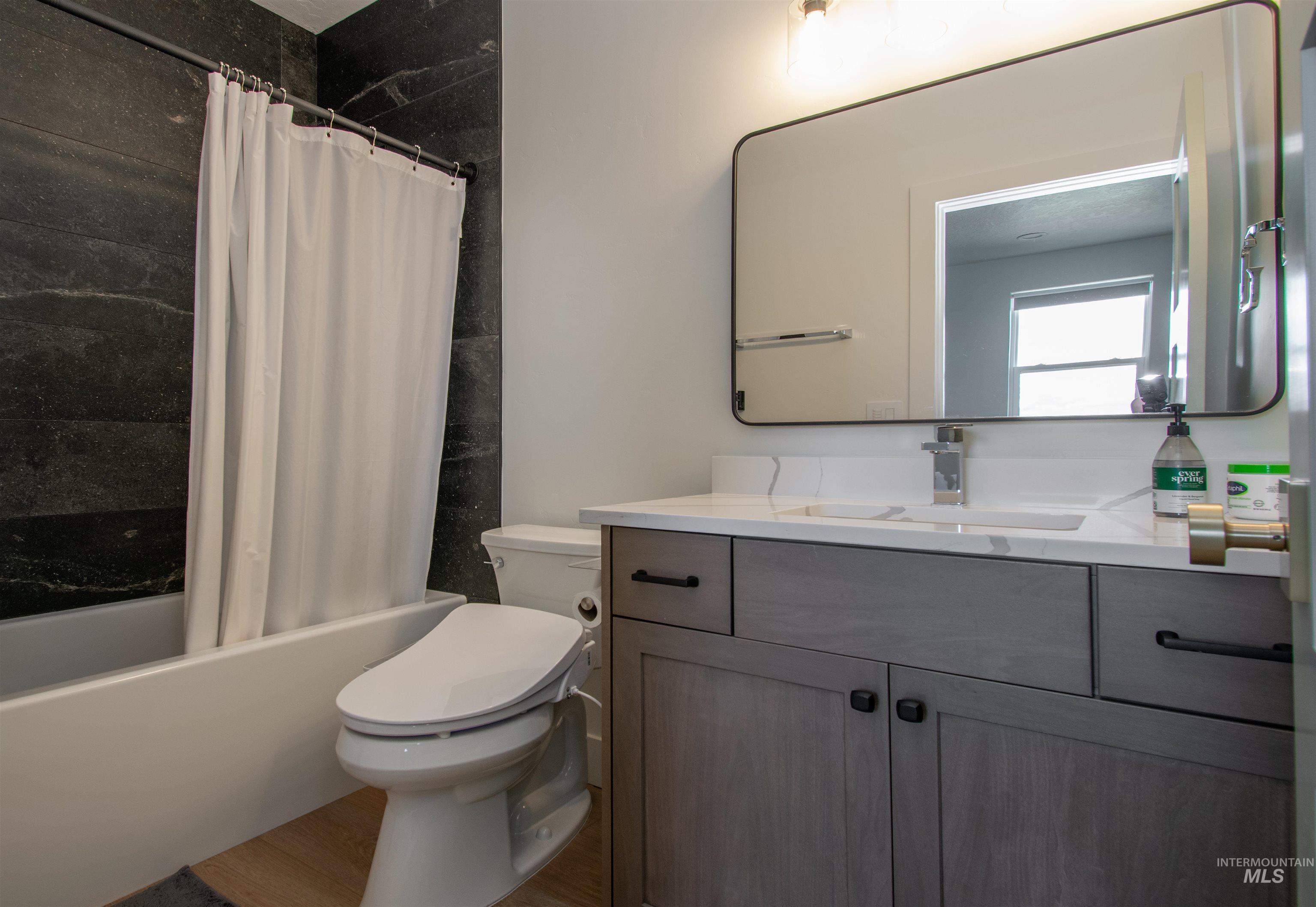44 Big Moose Road McCall, ID 83638 - Photo 35 of 50 Bathroom featuring a grey wood-finish vanity with a white countertop and integrated sink, a rectangular mirror, a bathtub with dark stone-look tile surround, and light wood-finish flooring