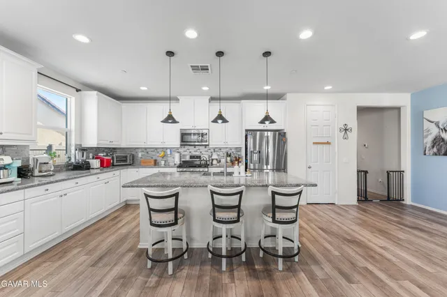 a kitchen with stainless steel appliances kitchen island granite countertop a wooden floor and white cabinets