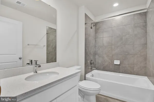 a bathroom with a granite countertop bathtub shower sink vanity mirror and toilet