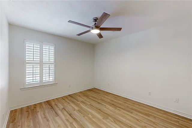 an empty room with wooden floor ceiling fan and windows