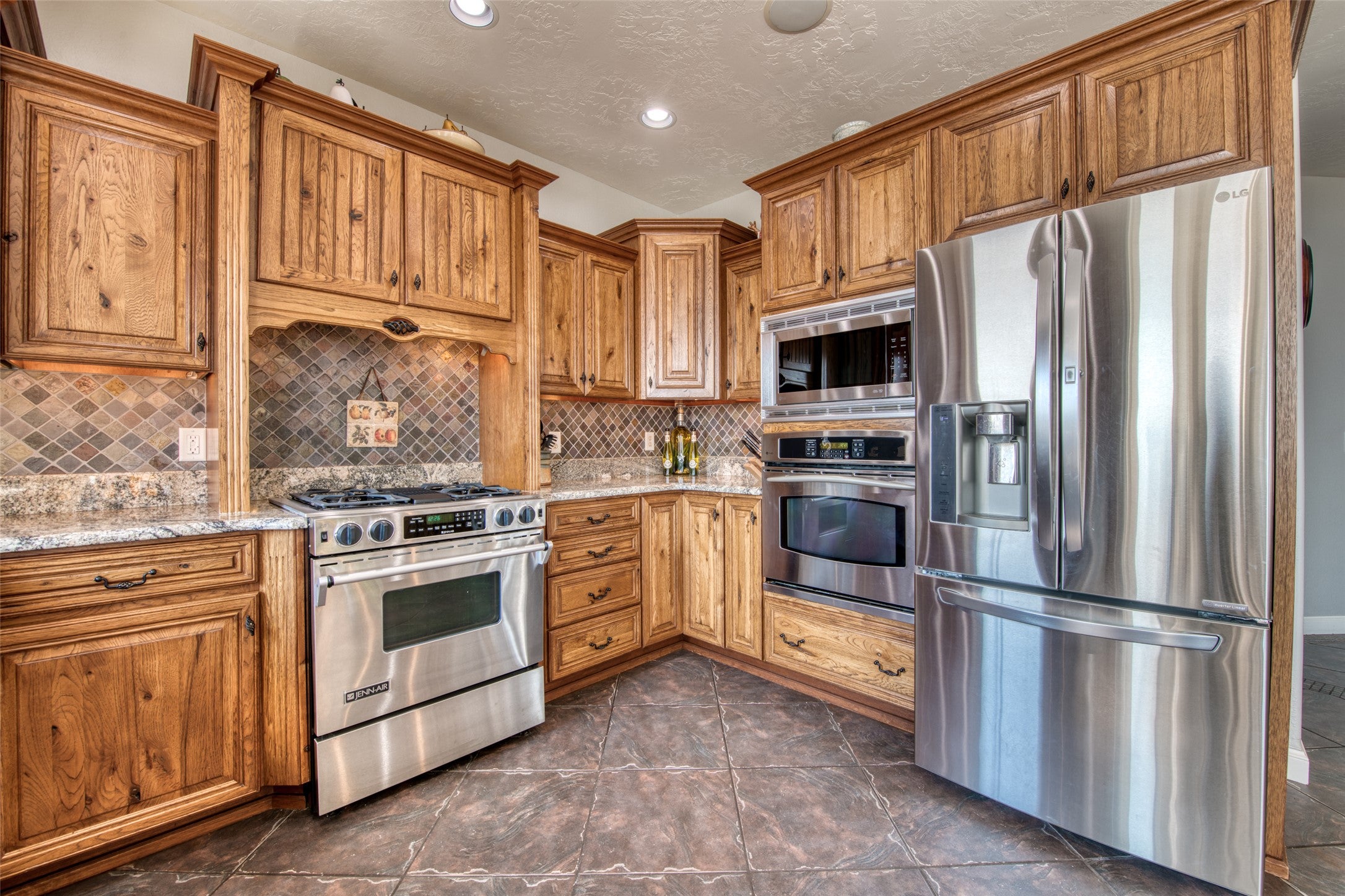 16374 Folsom Road Florence, MT 59833 - Photo 28 of 98 Kitchen with appliances with stainless steel finishes, brown cabinets, decorative backsplash, light stone countertops, and a textured ceiling