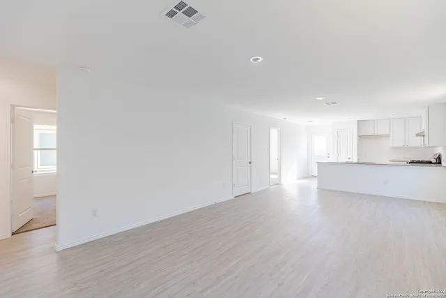 a view of an empty room and kitchen with wooden floor