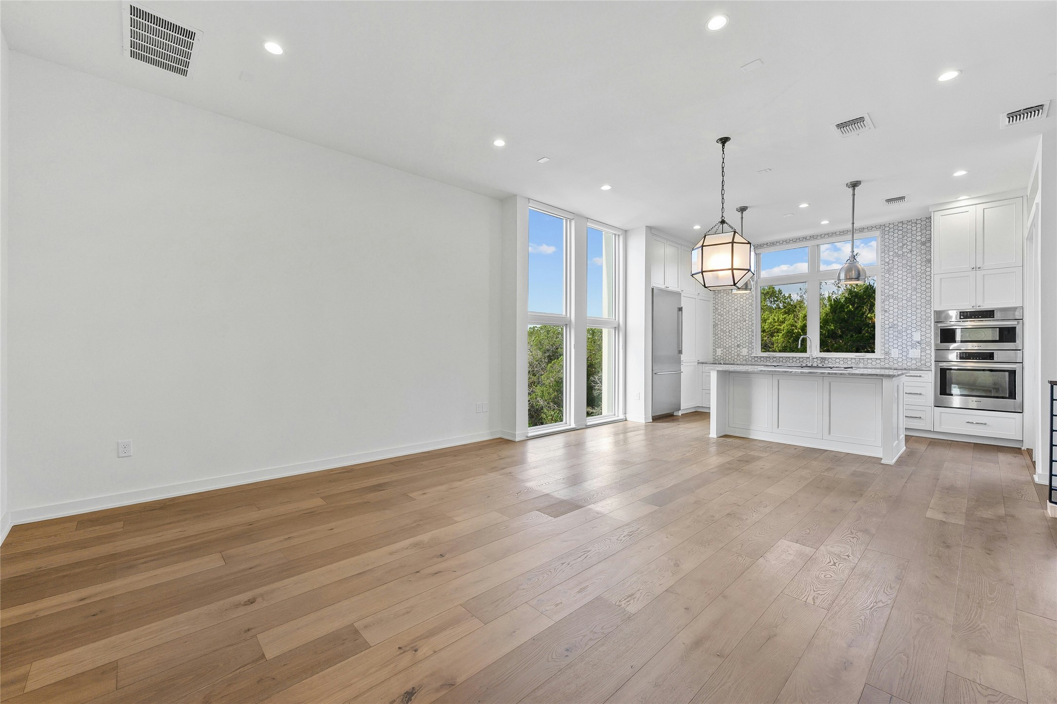 2518 Sutherland Street Austin, TX 78746 - Photo 5 of 30 A well-lit, open-concept living space seamlessly flows into a modern kitchen, featuring pristine hardwood flooring throughout.
