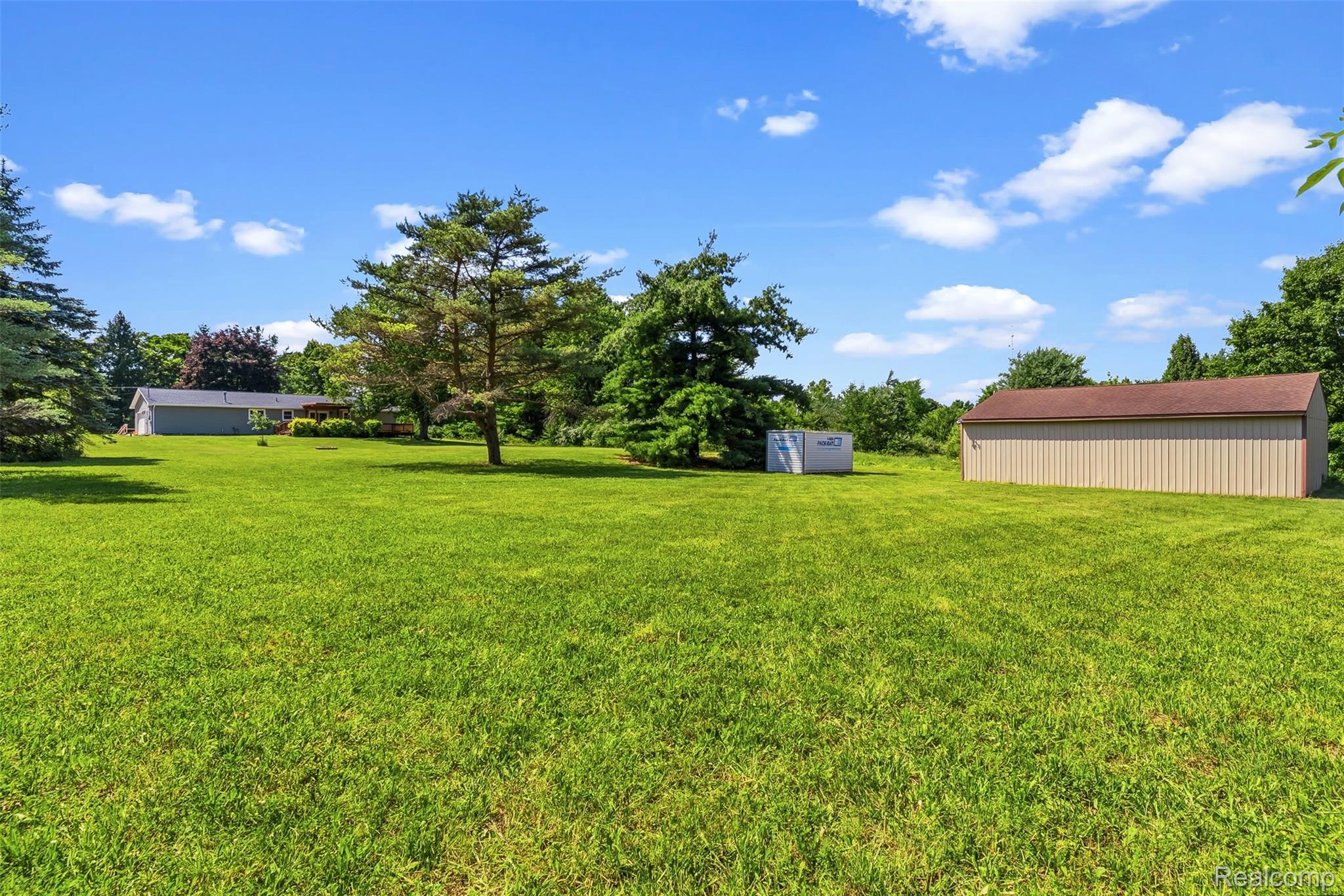 9200 Hickory Ridge Road Holly, MI 48442 - Photo 26 of 33 Expansive green lawn with mature trees, a detached storage building with a brown roof, and a single-story residence in the background