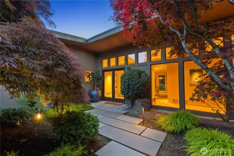 a view of house with a large tree and flower plants