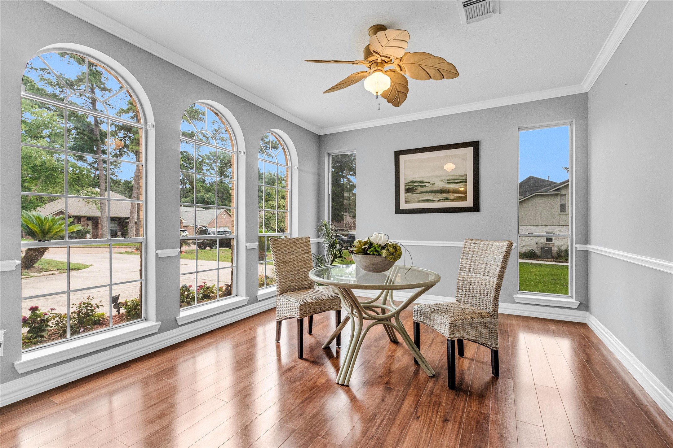 23 Alba Road Montgomery, TX 77356 - Photo 9 of 37 This bright, inviting dining area features large arched windows, offering ample natural light. The space includes elegant wood flooring, a ceiling fan with a leaf design, and a cozy table setup, perfect for intimate meals.