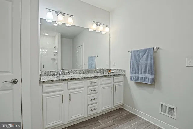 a bathroom with a granite countertop double vanity sink a mirror and shower