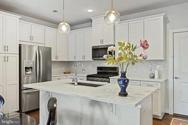 a kitchen with stainless steel appliances a sink a refrigerator a stove a oven a dining table and chairs with wooden floor