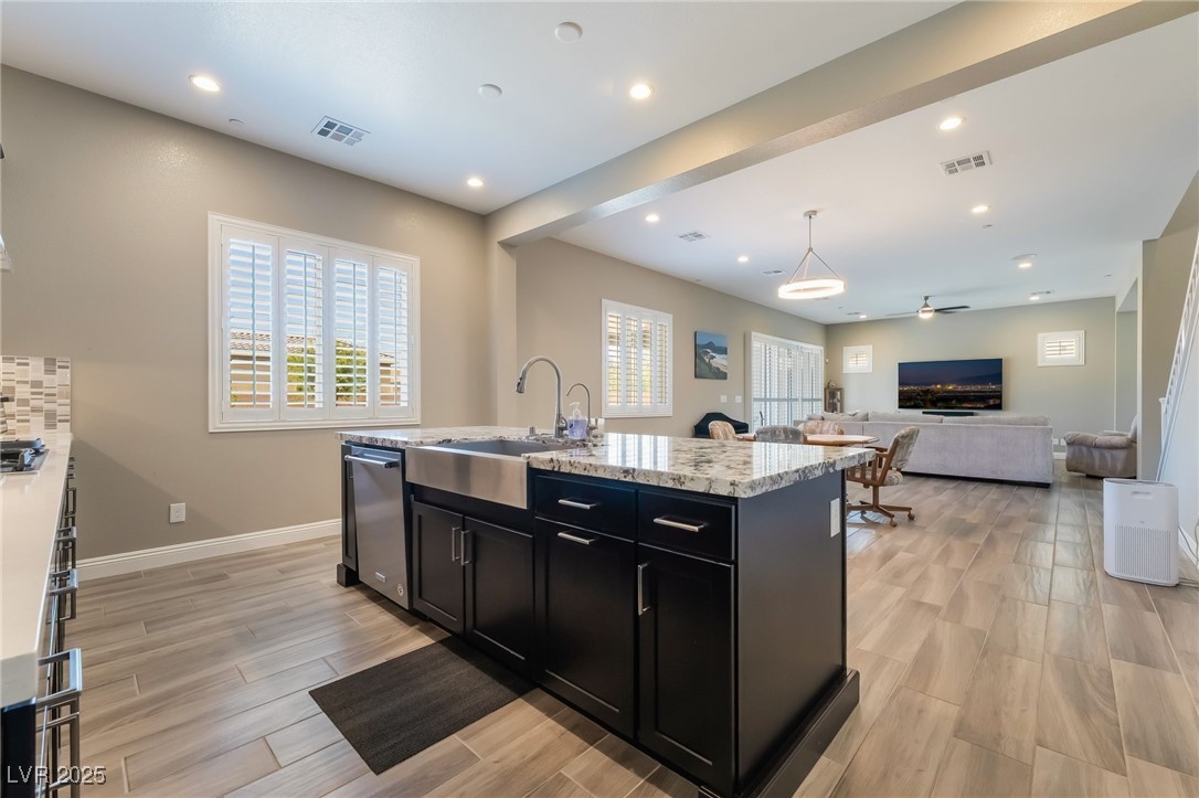 2575 Hazelburn Drive Henderson, NV 89044 - Photo 14 of 65 Kitchen with dark cabinets, stainless steel dishwasher, light wood finished floors, a center island with sink, and light stone countertops