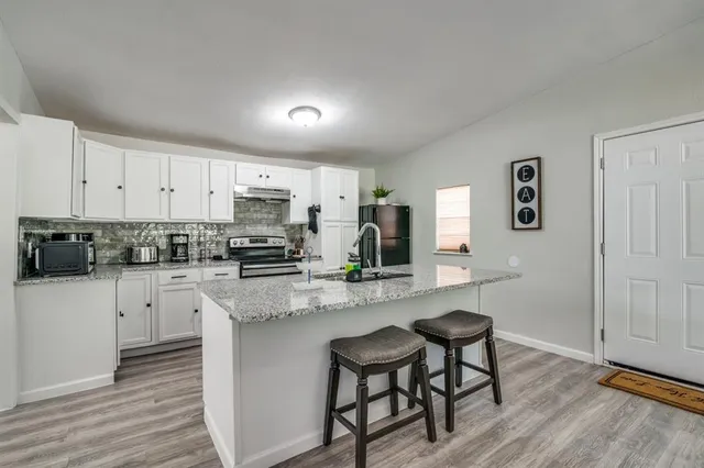 a kitchen with stainless steel appliances granite countertop a stove top oven a sink a refrigerator white cabinets and wooden floor