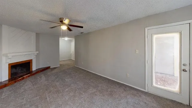 a view of an empty room with chandelier fan and fire place