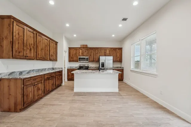a large kitchen with stainless steel appliances kitchen island granite countertop a large counter top cabinets and a window