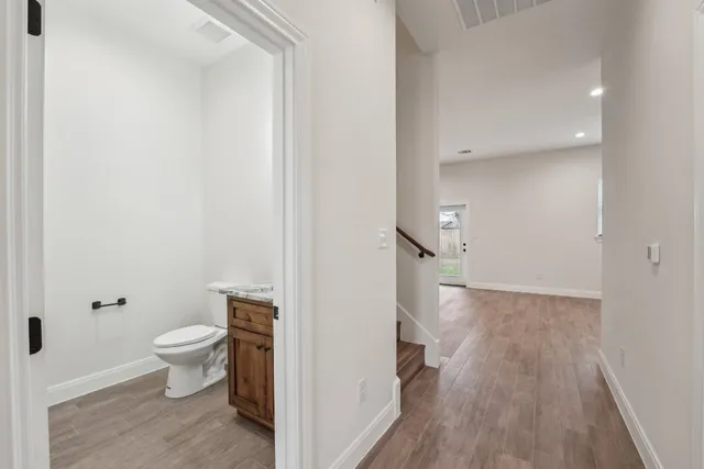 a view of a hallway with wooden floor and a toilet