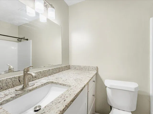 a bathroom with a granite countertop sink a toilet and a mirror
