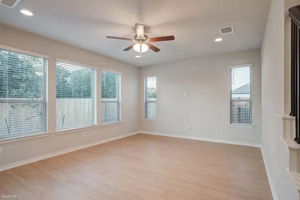 an empty room with chandelier fan and windows