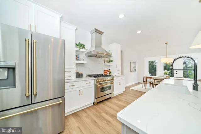 a large kitchen with stainless steel appliances a stove a refrigerator a oven and white cabinets with wooden floor