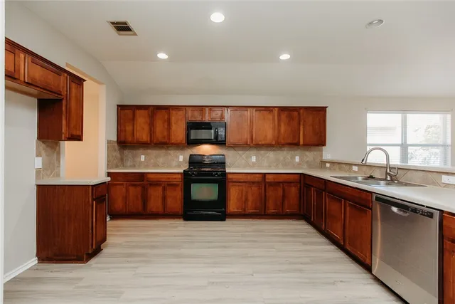 a large kitchen with stainless steel appliances granite countertop wooden cabinets a stove a sink and a microwave