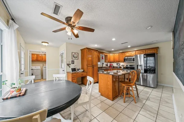 a dining room with stainless steel appliances kitchen island granite countertop a table chairs and a chandelier