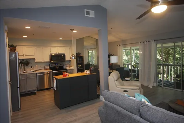 a living room with stainless steel appliances kitchen island granite countertop a refrigerator a stove top oven a sink with wooden floor and cabinets