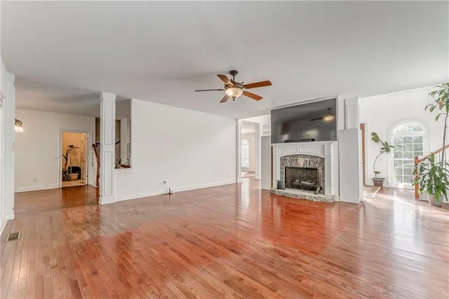 a view of a livingroom with a fireplace a ceiling fan and wooden floor
