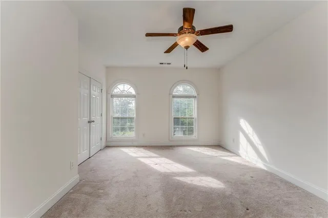 an empty room with chandelier fan and windows