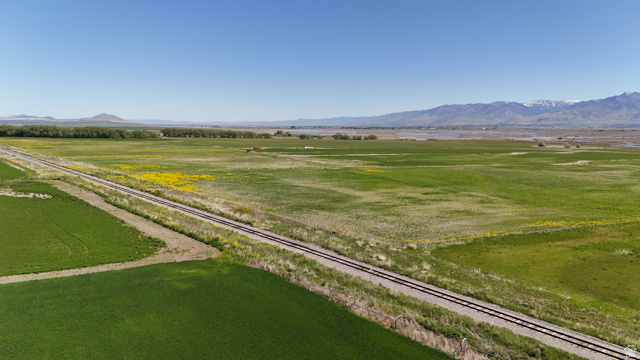 320 South 5400 West Logan, UT 84321 - Photo 26 of 42 Expansive agricultural land featuring a railway line, vibrant green fields, distant mountains, and a clear blue sky