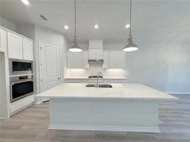 a large white kitchen with kitchen island a sink stainless steel appliances and cabinets
