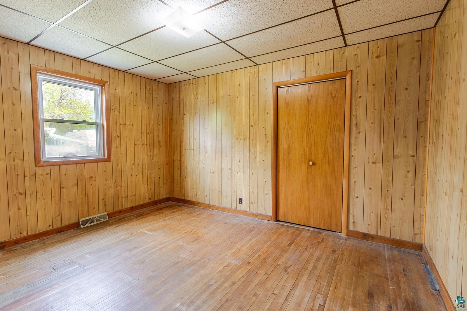 438 9th Street Cloquet, MN 55720 - Photo 14 of 27 Room featuring wood-finish paneling, wood-finish flooring, a double-hung window, a flush mount ceiling light fixture, and a wood-finish interior door