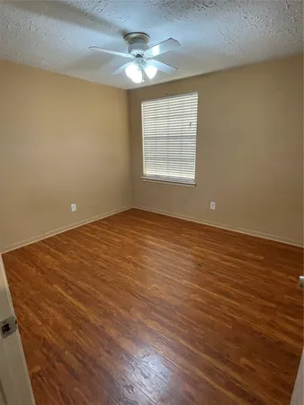 an empty room with wooden floor chandelier fan and windows