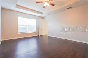 an empty room with wooden floor chandelier fan and windows