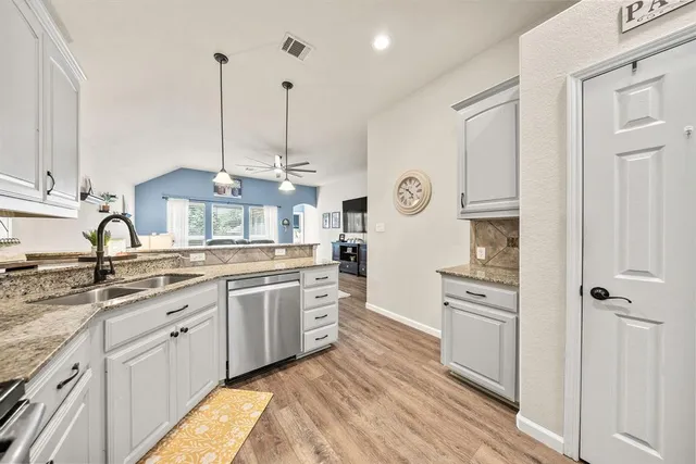 a kitchen with stainless steel appliances granite countertop a stove a sink and white cabinets with wooden floor