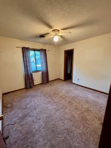 an empty room with chandelier fan and windows