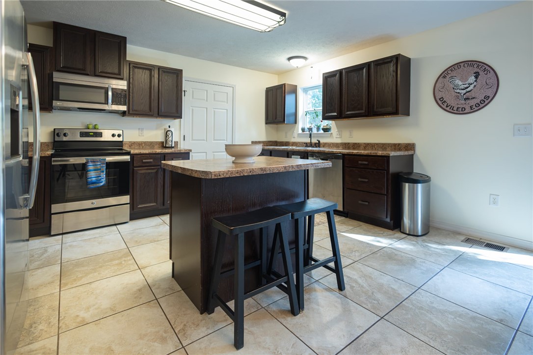 437 Gip Annie Road West Harrison, AR 72601 - Photo 7 of 21 Kitchen featuring dark wood cabinetry, stainless steel appliances, a center island with seating, light-toned tile flooring, and laminate countertops